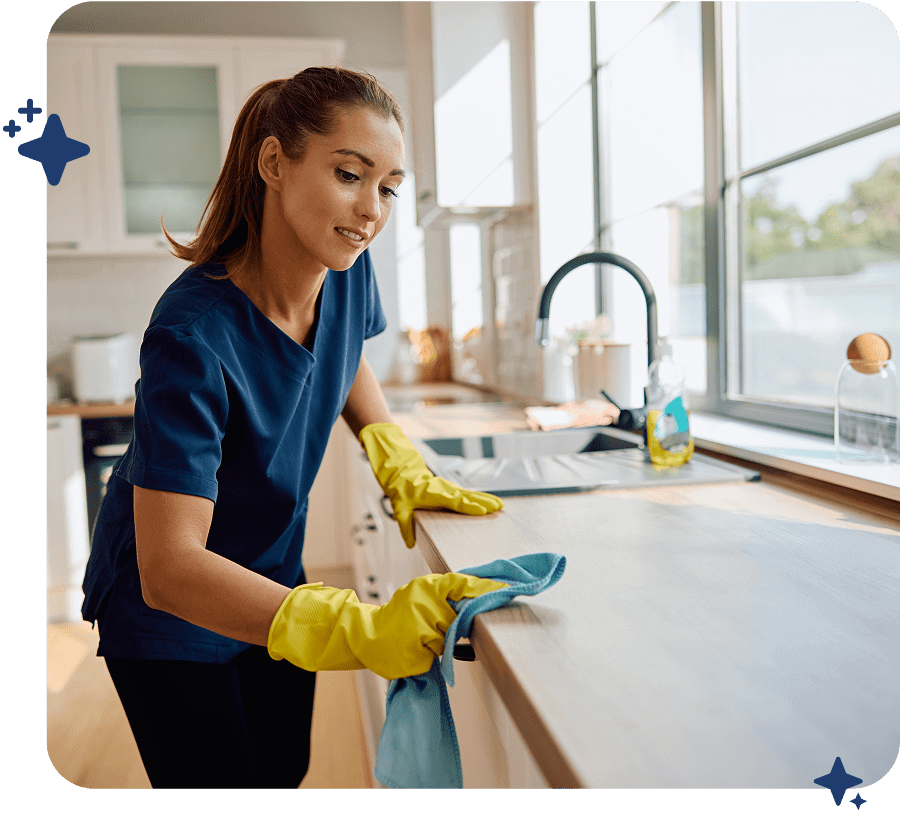 Woman cleaning a kitchen countertop with gloves and cloth.