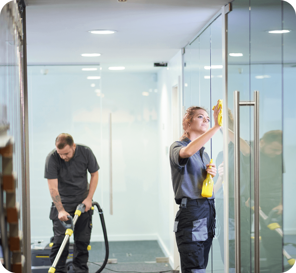 Two workers cleaning glass walls in an office space.